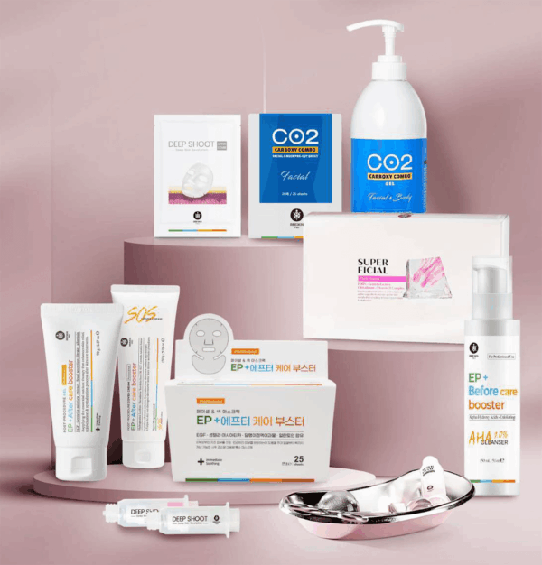 Zestaw produktów do pielęgnacji skóry ułożony na różowych podium: butelka z pompką i niebieską etykietą CO2, pudełka maseczek i opakowania Deep Shoot oraz Super Facial, tubki i ampułki oraz metalowa miseczka z akcesoriami.
